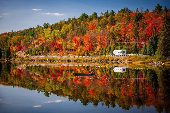 White RV parked by a lake surrounded by vibrant fall colors